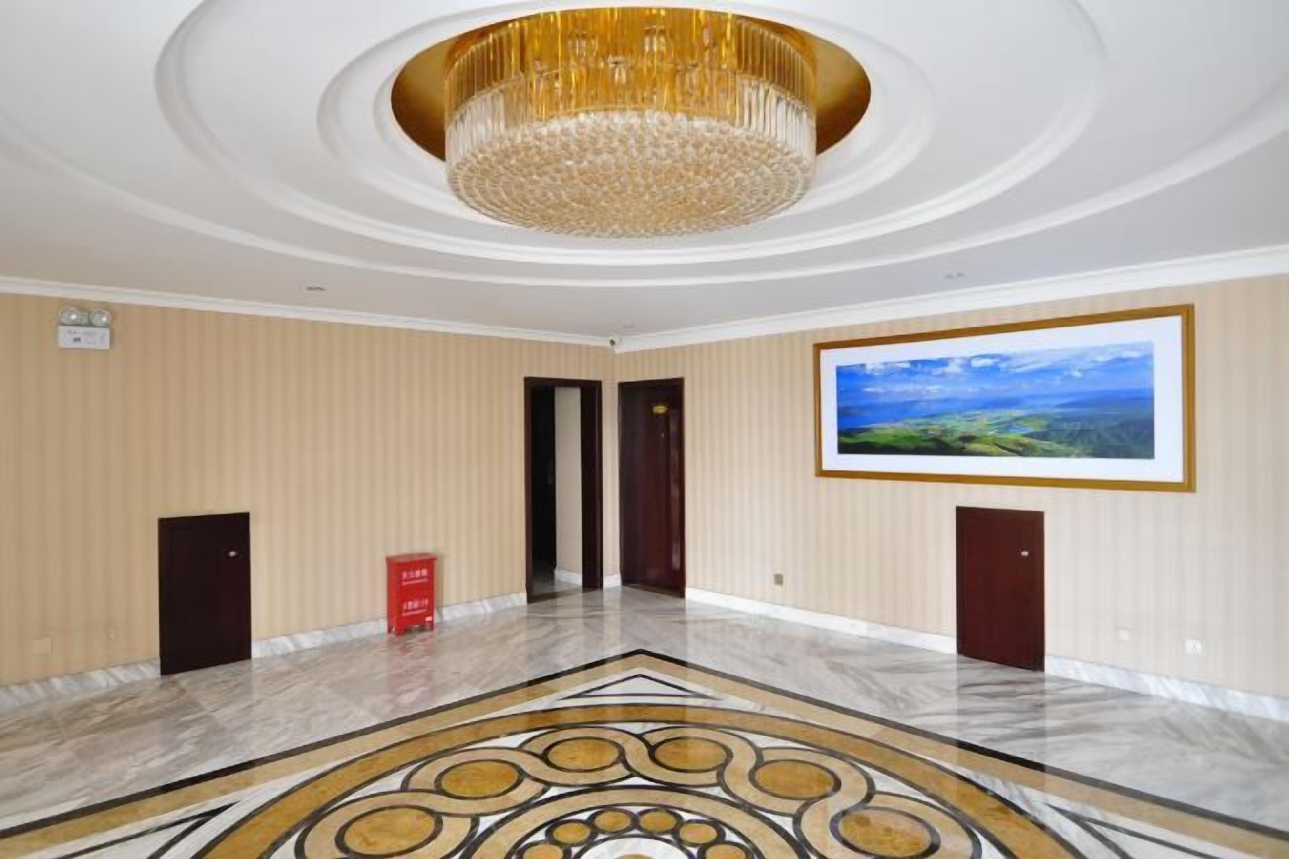 Un hall d’entrée spacieux, doté d’un sol en marbre, d’un grand lustre et d’un tableau représentant un paysage, encadré et accroché au mur.