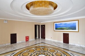 Un hall d’entrée spacieux, doté d’un sol en marbre, d’un grand lustre et d’un tableau représentant un paysage, encadré et accroché au mur.