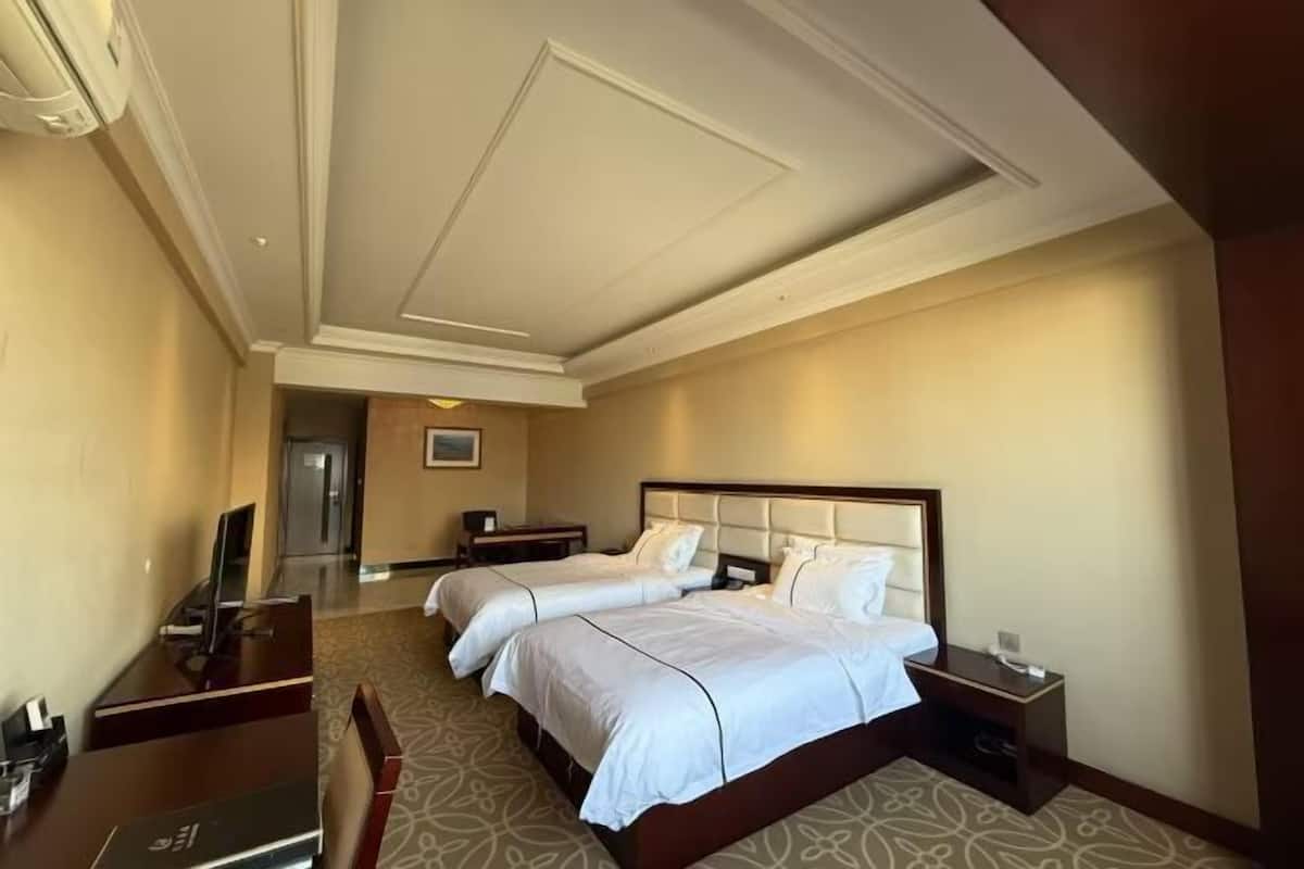 Ein Hotelzimmer mit zwei Betten, einem Schreibtisch, einem Stuhl, einem Fernseher und einer Tür zu einem Flur.