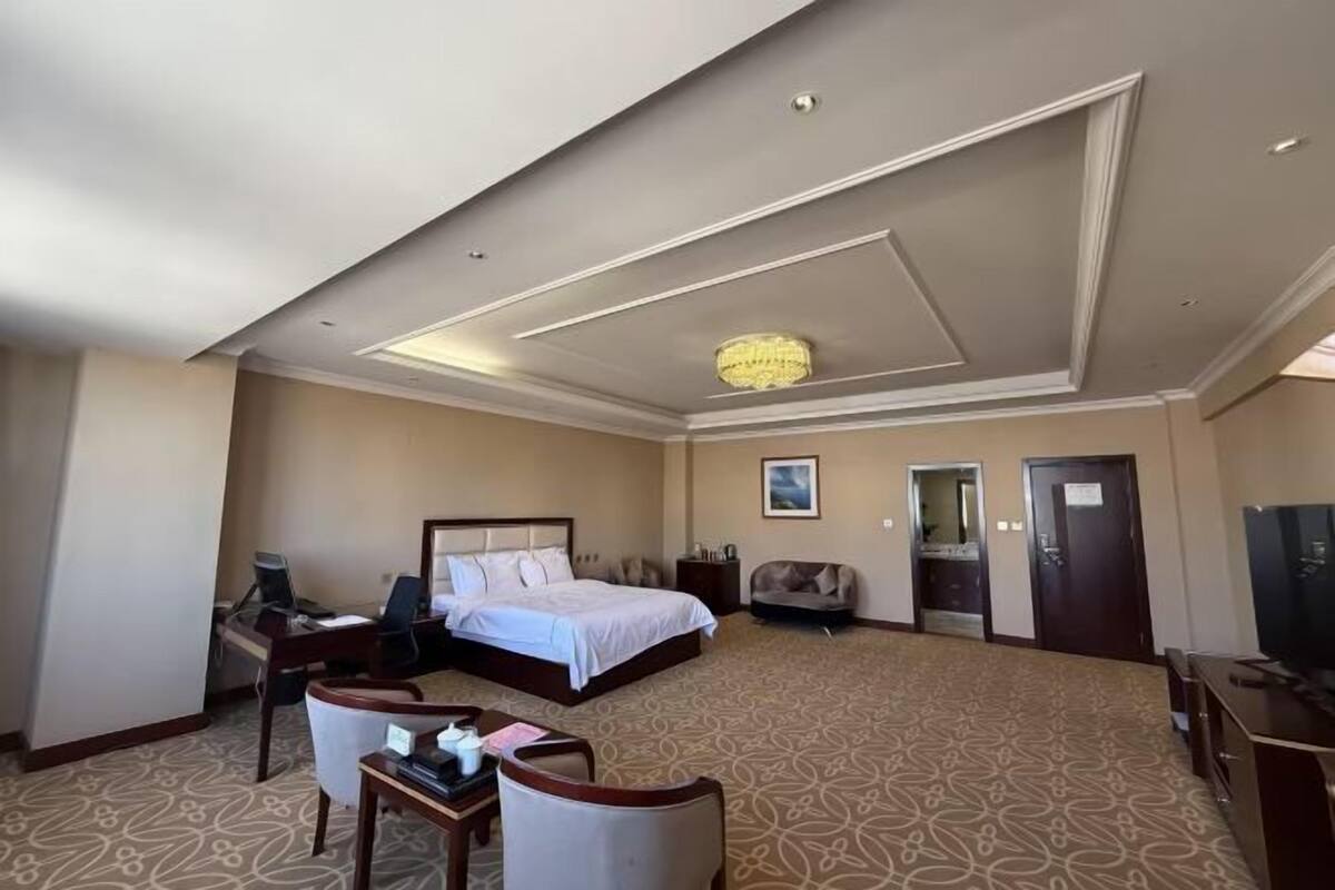 Ein Hotelzimmer mit einem großen Bett, einem Schreibtisch mit Stuhl, einem Fernseher und einer Chandelier.