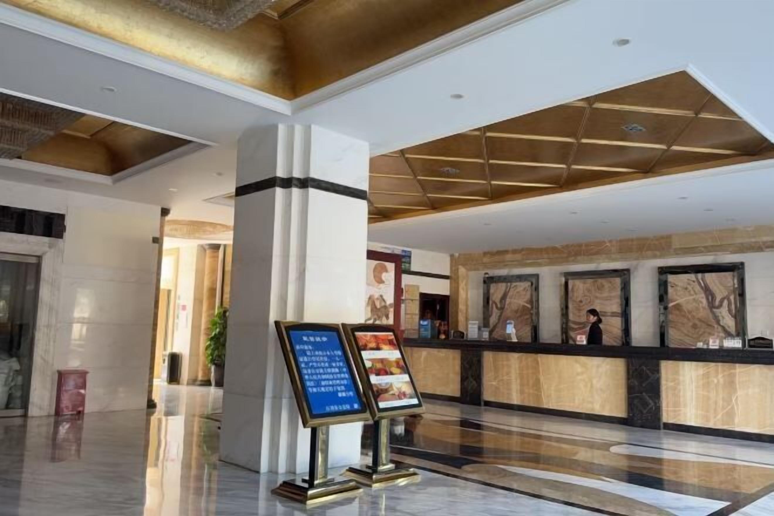 A hotel lobby with a reception desk, a large column, and a digital menu board.