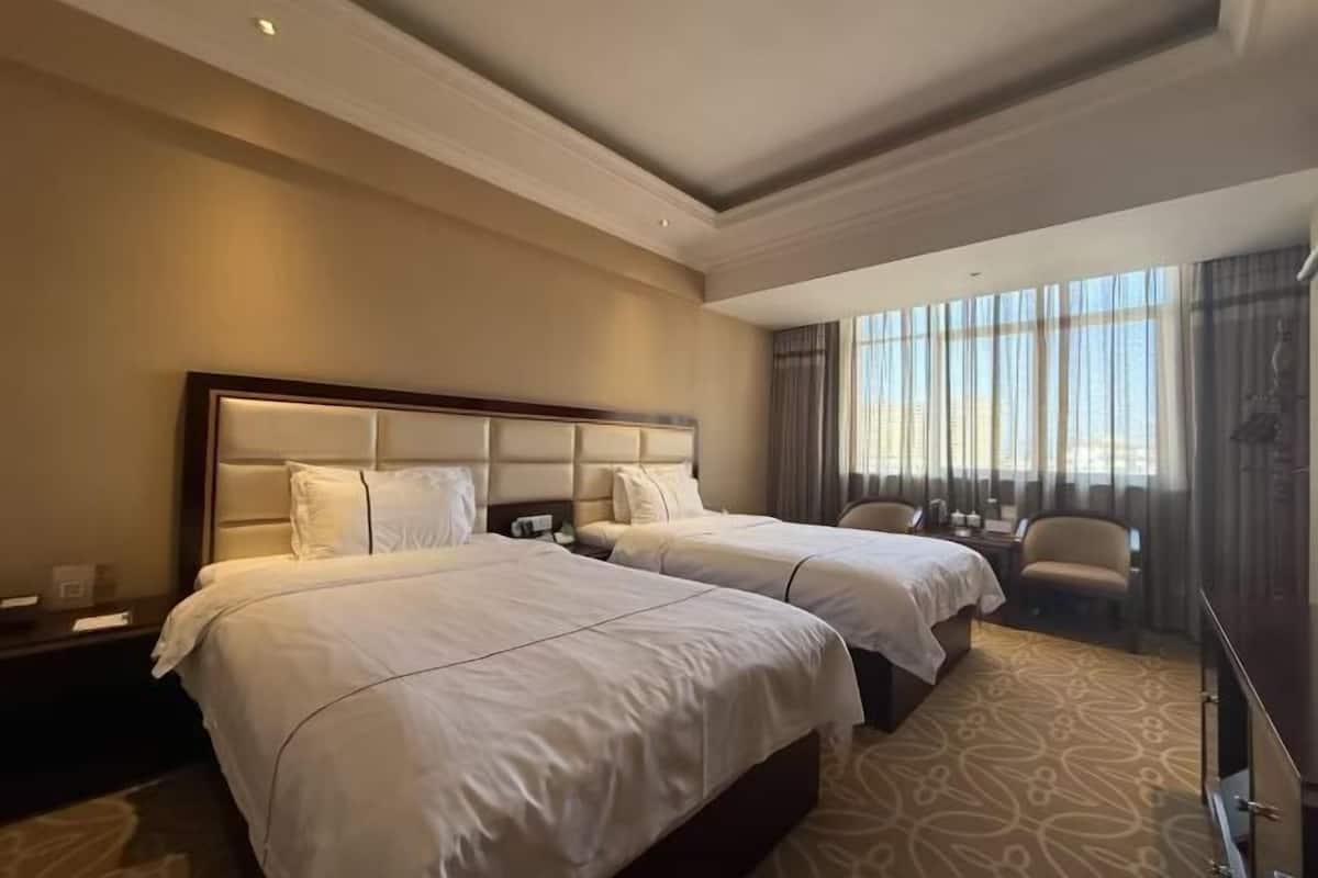 Ein Hotelzimmer mit zwei Betten, einem Schreibtisch, einem Sessel und einem großen Fenster mit Vorhängen.