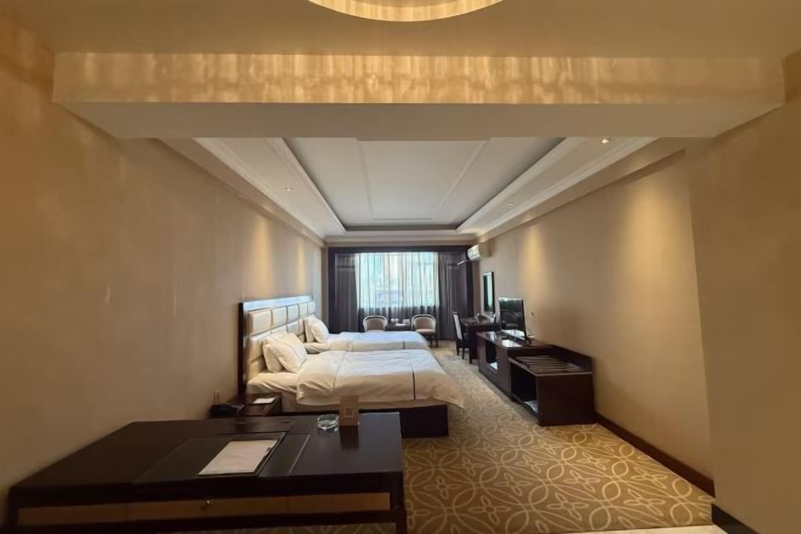Habitación de hotel con dos camas, un escritorio, un televisor y una zona de estar con vistas a la ciudad.