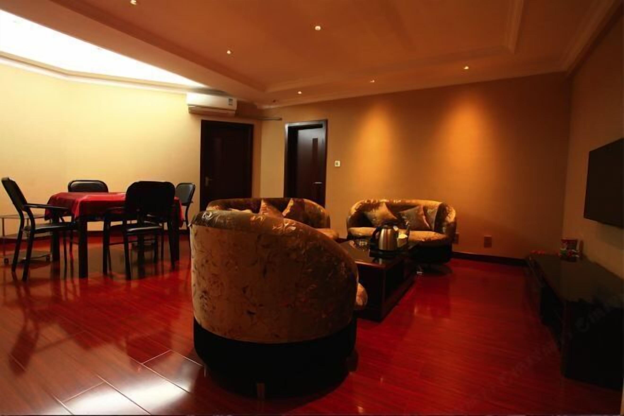 A spacious living room with a red carpet, a large armchair, a sofa, and a dining area with chairs and a table.