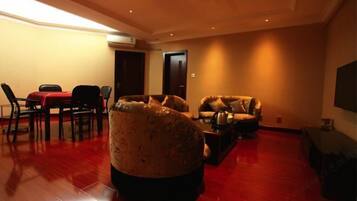 A spacious living room with a red carpet, a large armchair, a sofa, and a dining area with chairs and a table.