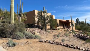 Woestijnlandschap met verschillende cactussen en een gebouw met een plat dak en beige muren.