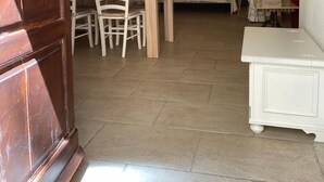 A room with a wooden dining table, white chairs, a bed with a headboard, and a white cabinet. - SUITE DI SAN FRANCESCO (Grottaglie)