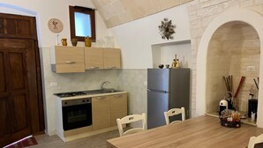 A compact kitchen with a dining area, a stove, oven, refrigerator, and a small window. - SUITE DI SAN FRANCESCO (Grottaglie)