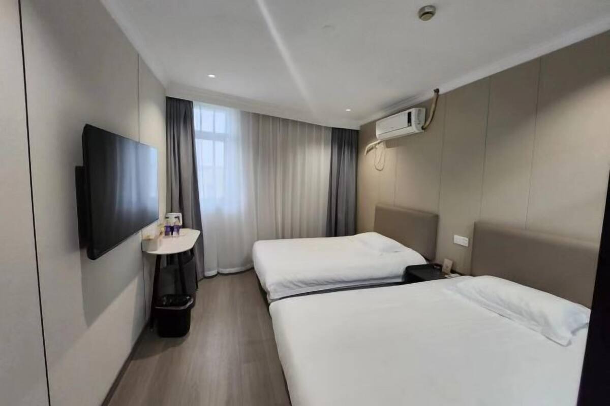 Une chambre d’hôtel avec deux lits, une télévision, une petite table et une fenêtre avec des rideaux.