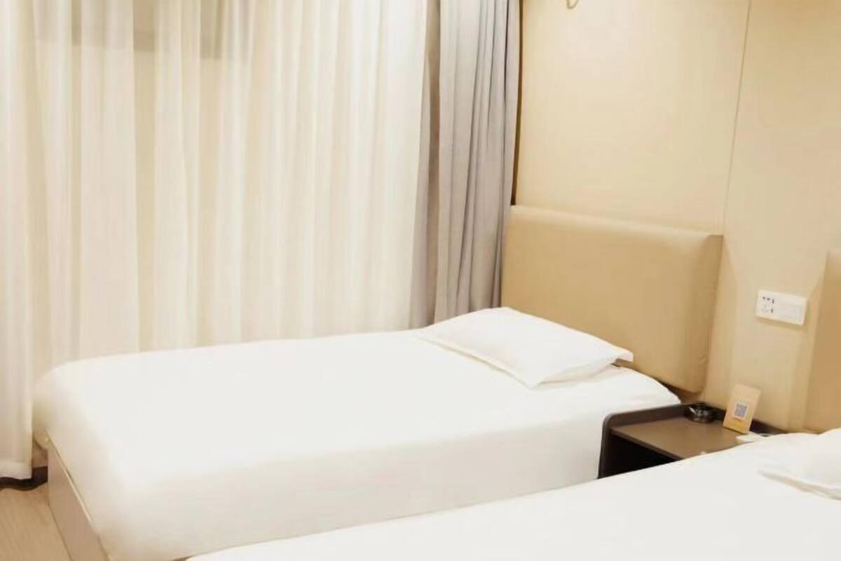 Une chambre d’hôtel avec deux lits simples, une table de chevet avec une lampe et une fenêtre avec des rideaux.