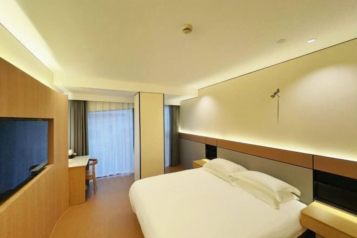 Une chambre d’hôtel avec un lit, une télévision, un bureau et une grande fenêtre avec des rideaux.