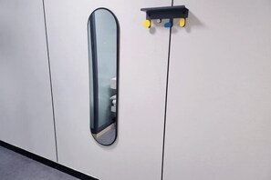 Un mur blanc orné d’un miroir et d’une petite étagère sur laquelle sont posés des objets jaunes et bleus.