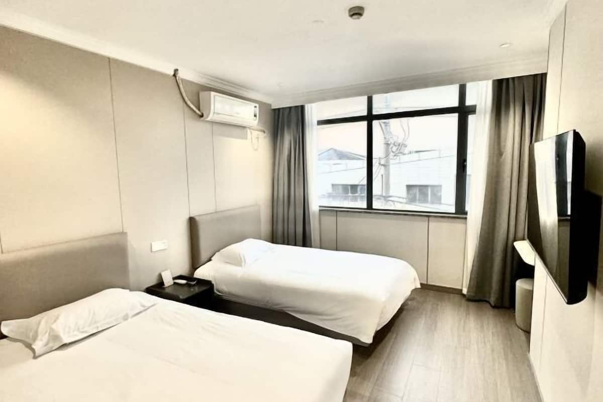 Une chambre d’hôtel avec deux lits, une télévision, un appareil de climatisation et une fenêtre avec des rideaux.