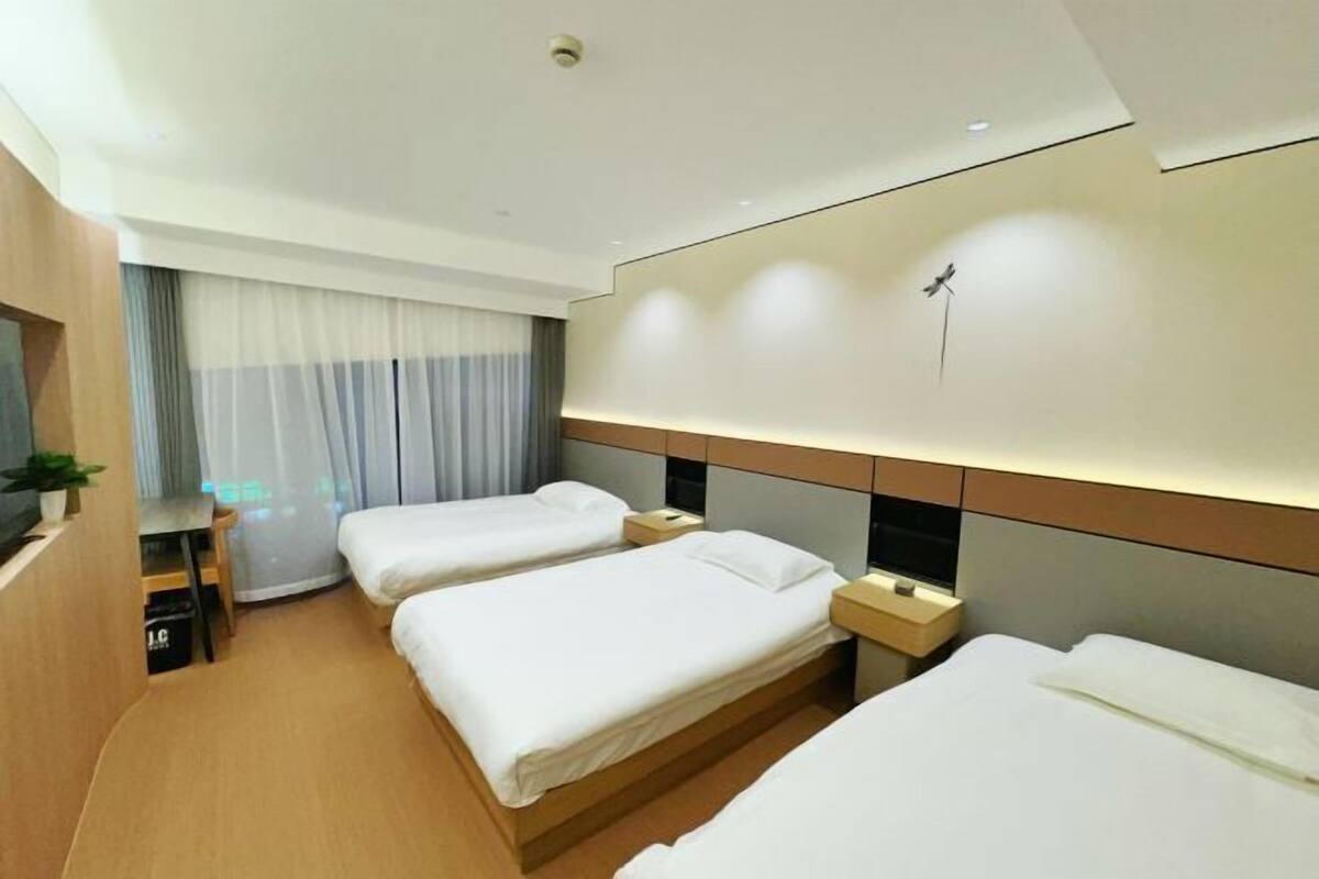 Une chambre d’hôtel avec deux lits simples, un bureau, une chaise, une télévision et une fenêtre avec des rideaux.