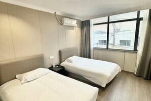 A hotel room with two beds, a window with curtains, an air conditioning unit, and a nightstand. - Shanghai Jincheng Hotel (Zhujiajiao Ancient Town) (Shanghai)