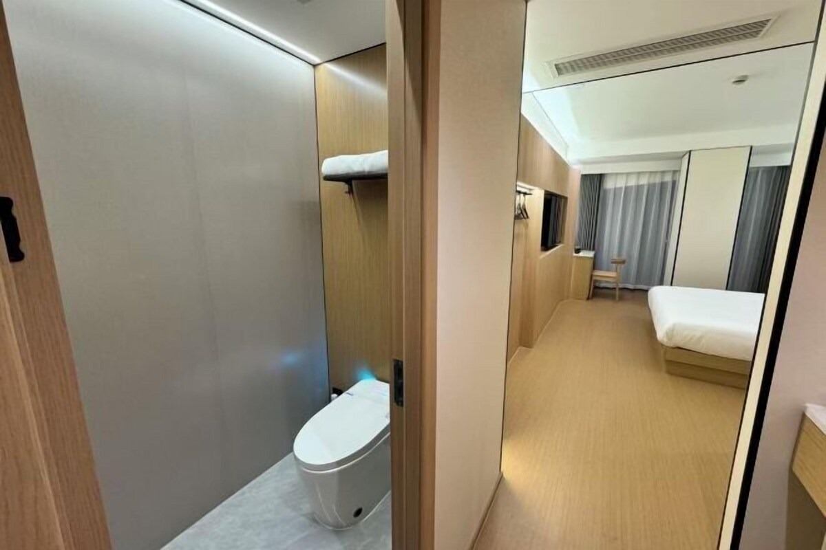 A compact hotel room with a wooden wardrobe, a small toilet, a bed, and a bedside table.