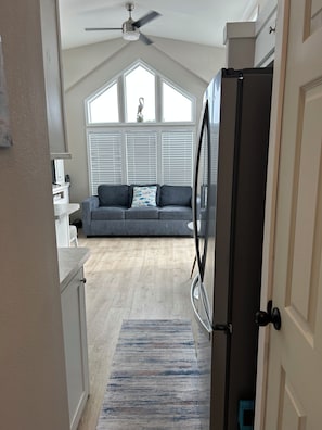 A kitchen with a refrigerator, a dining area with a table and chairs, and a seating area with a sofa and a window with blinds. - Keys Paradise! (Key Largo)