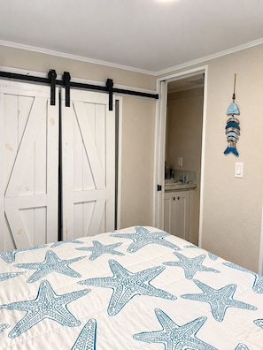 A bedroom with a bed featuring a starfish pattern, a sliding door, and a hanging fish decoration. - Keys Paradise! (Key Largo)