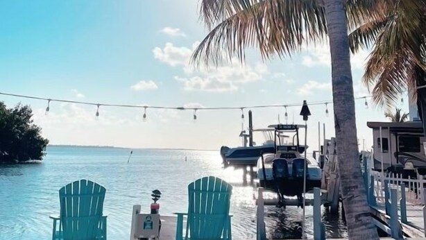 A beach with two green chairs, a palm tree, and boats in the background. - Keys Paradise! (Key Largo)