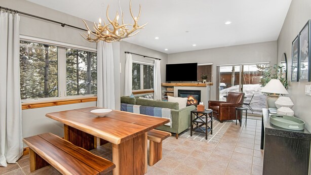 A modern living room with a wooden dining table, benches, a sofa, and a fireplace.