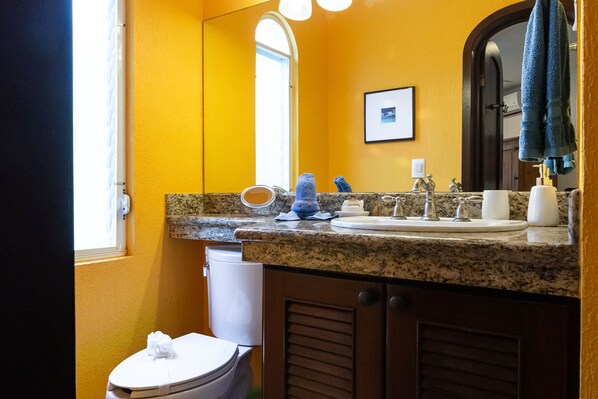 A bathroom with a granite countertop, a sink, a mirror, and a toilet.