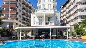 A hotel with a pool, multiple balconies, and a covered area with tables and chairs.