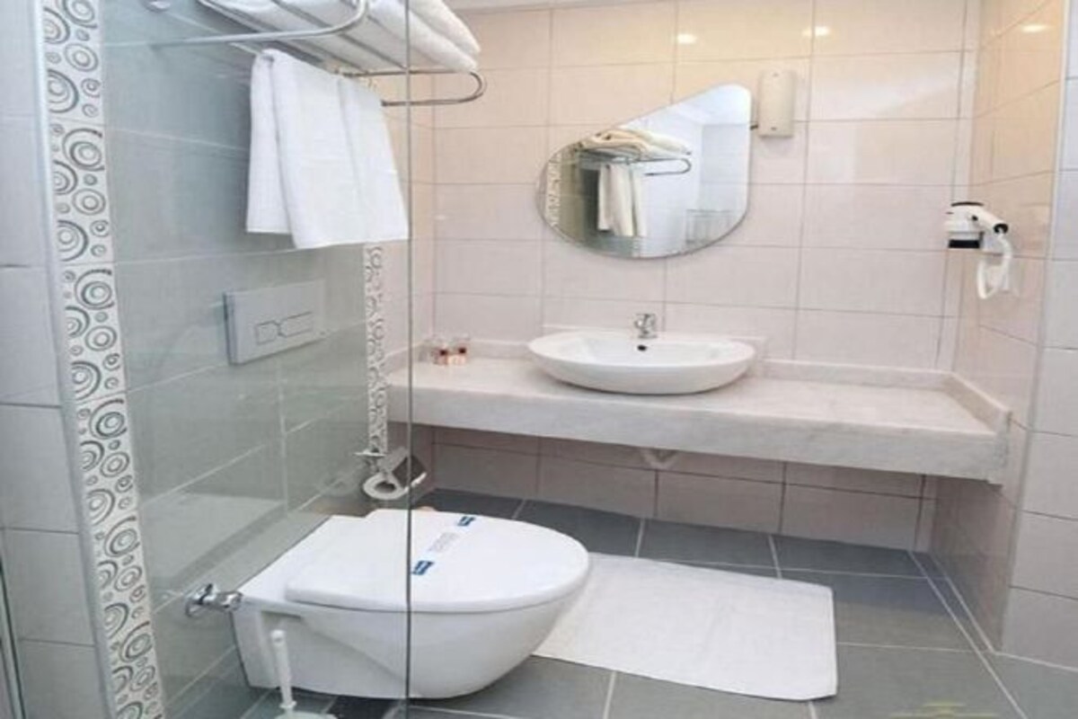 A modern bathroom with a glass shower enclosure, a white toilet, a sink with a mirror above it, and a towel rack.