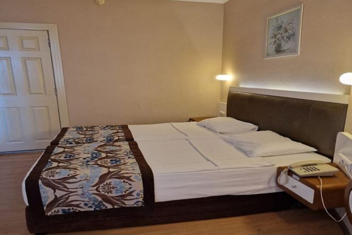 A neatly made bed with a patterned bedspread, a bedside telephone, and a wall-mounted light fixture.