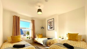 Ein Hotelzimmer mit zwei Betten, einem Fenster mit Vorhängen, einem gerahmten Bild an der Wand und einem kleinen Tisch mit einer Lampe.