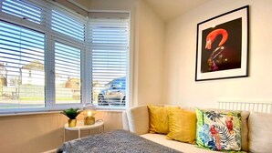 Ein Schlafzimmer mit einem Bett, einem Fenster mit Jalousien, einem Nachttisch mit Lampe und einem Wandbild.