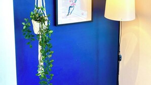 Eine blaue Wand mit einem hölzernen Regal, das eine kleine Pflanze und ein gerahmtes Bild beherbergt.