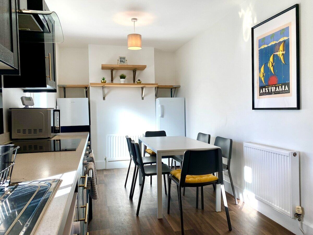 A modern kitchen with a dining area, featuring a white table, black chairs, and a wooden countertop.