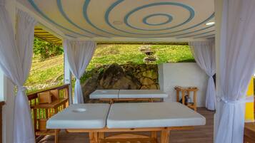 Un espace de bien-être comprenant deux tables de massage, un mur en pierre et une terrasse en bois.