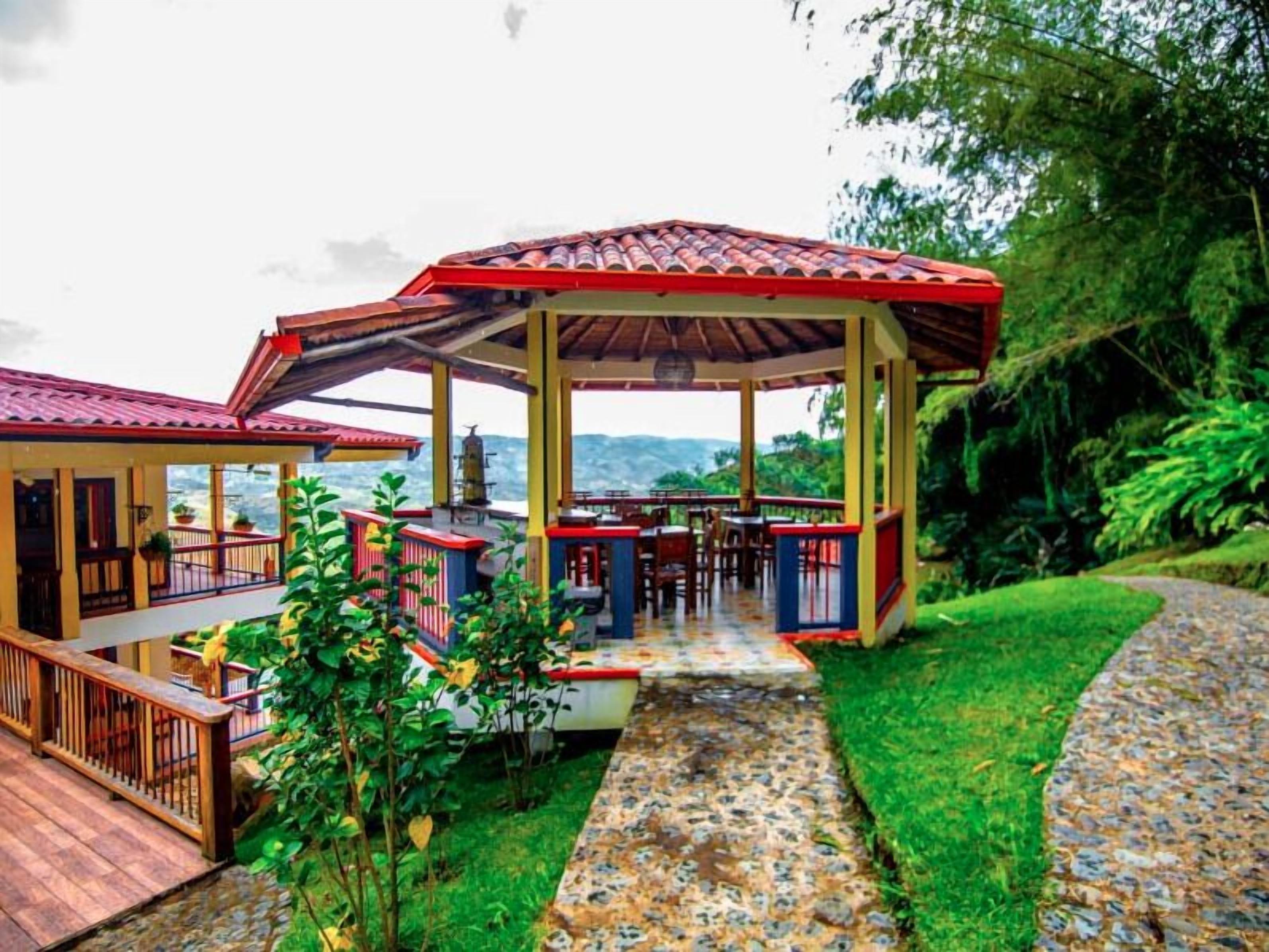 A covered outdoor area with a dining setup, a pathway, and lush greenery.
