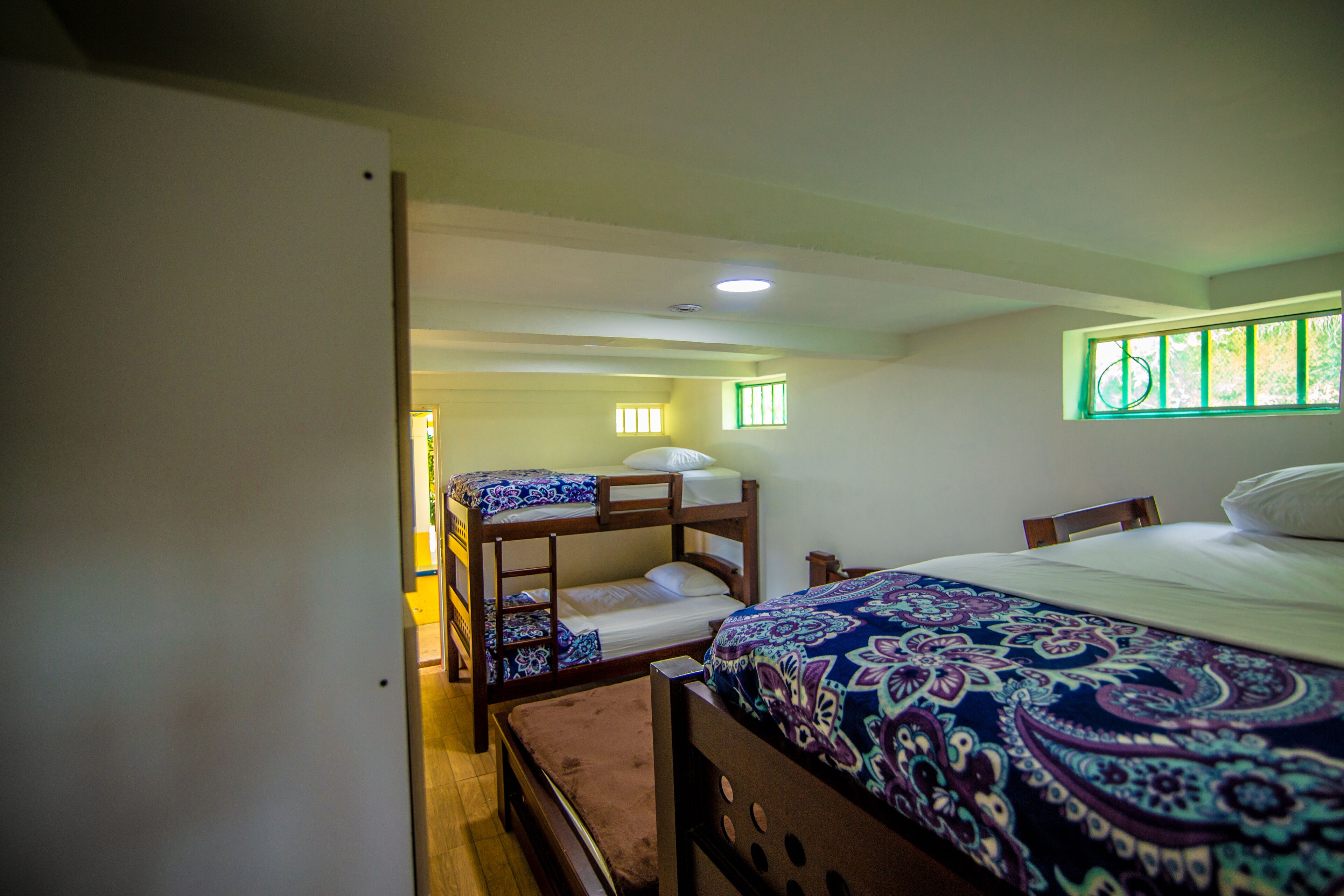 A room with bunk beds, a single bed, and a window with green bars.