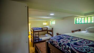 A room with bunk beds, a single bed, and a window with green bars.
