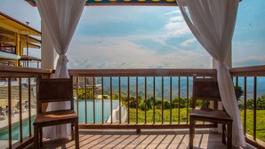 A balcony with two wooden chairs and a view of a pool and mountains. - Hotel Terra Belén (Belén de Umbría)