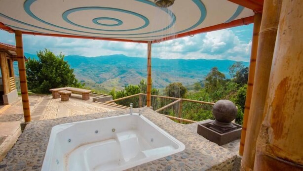 A hot tub with a stone floor, a bench, and a view of mountains. - Hotel Terra Belén (Belén de Umbría)