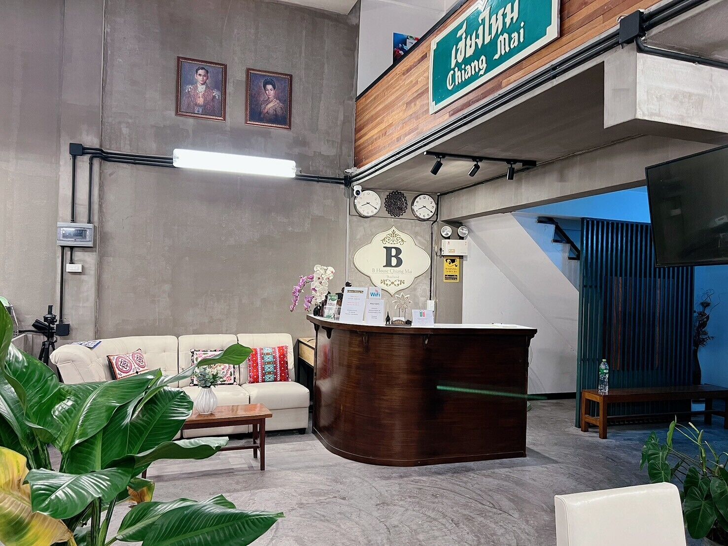 A reception area with a wooden reception desk, a sofa, and a coffee table. There are two clocks on the wall and a sign with the letter 'B'.