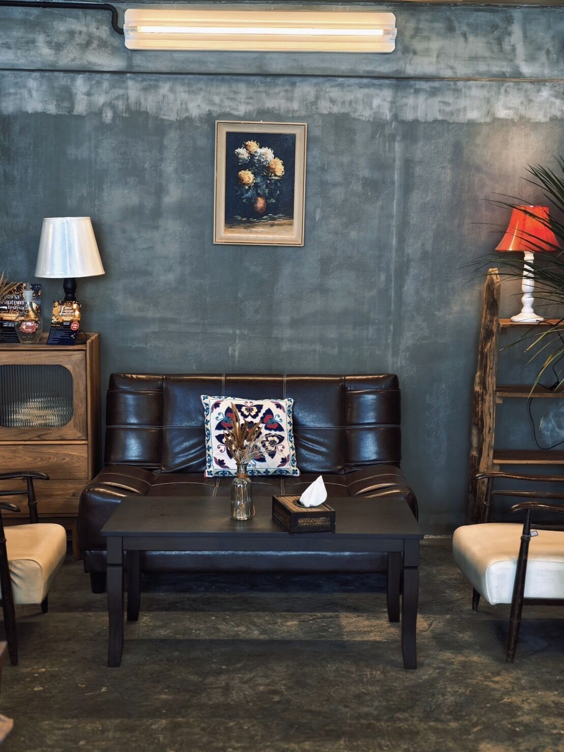 A modern living room with a dark leather sofa, a wooden coffee table, and a framed floral painting on the wall.