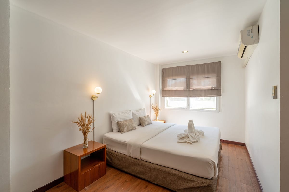 Un dormitorio con cama, lámparas de noche, mesita de noche y ventana con cortinas.