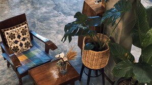 Ein gemütlicher Sitzbereich mit einem Holztisch, Stühlen und einer Kaffeekanne. Es befinden sich Blumentöpfe und eine Wanddekoration dort.