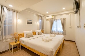 Ein Hotelzimmer mit zwei Betten, einem kleinen Tisch, einer Klimaanlage und einem an der Wand montierten Fernseher.