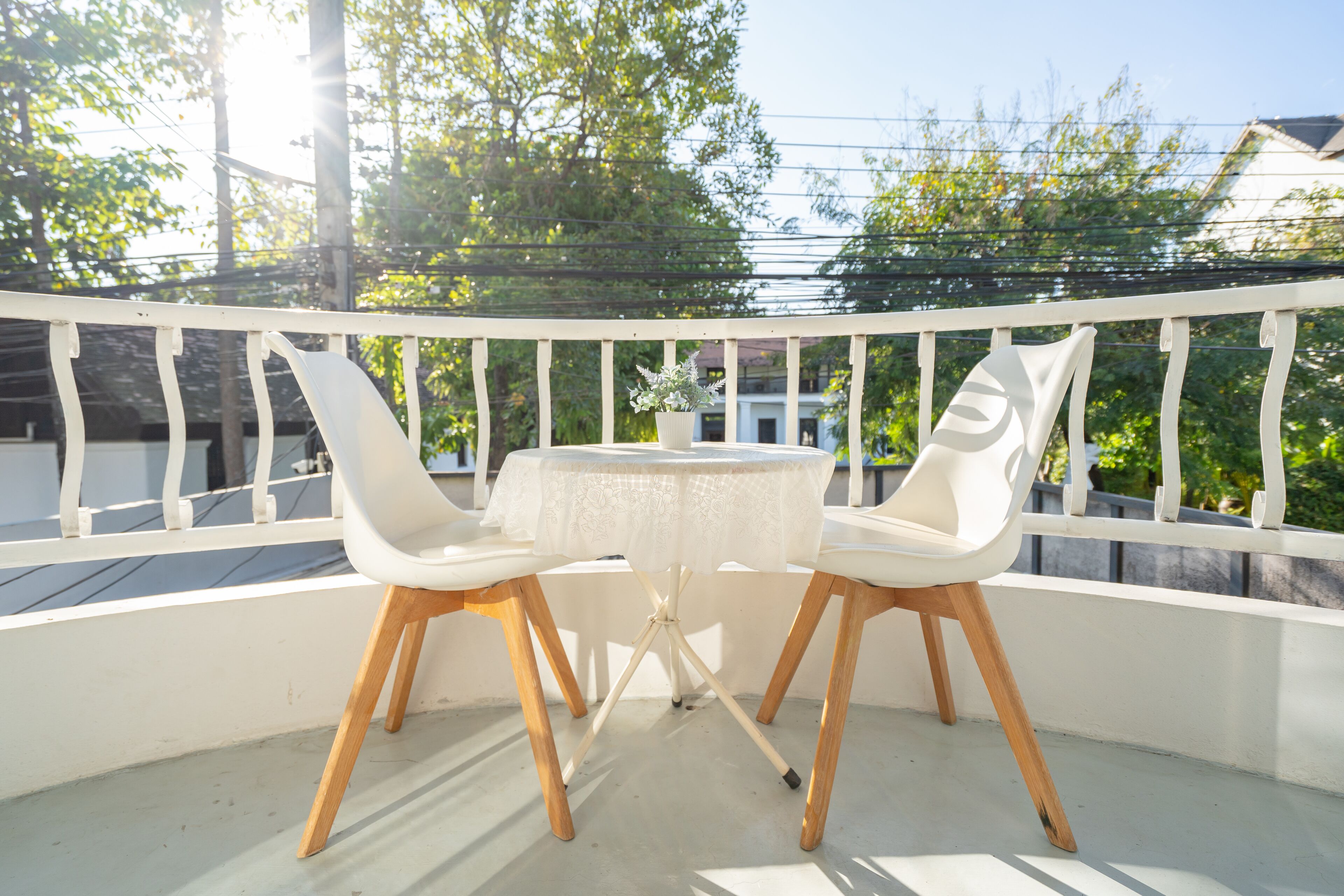 A balcony with a white railing, a small round table, and two white chairs with wooden legs.
