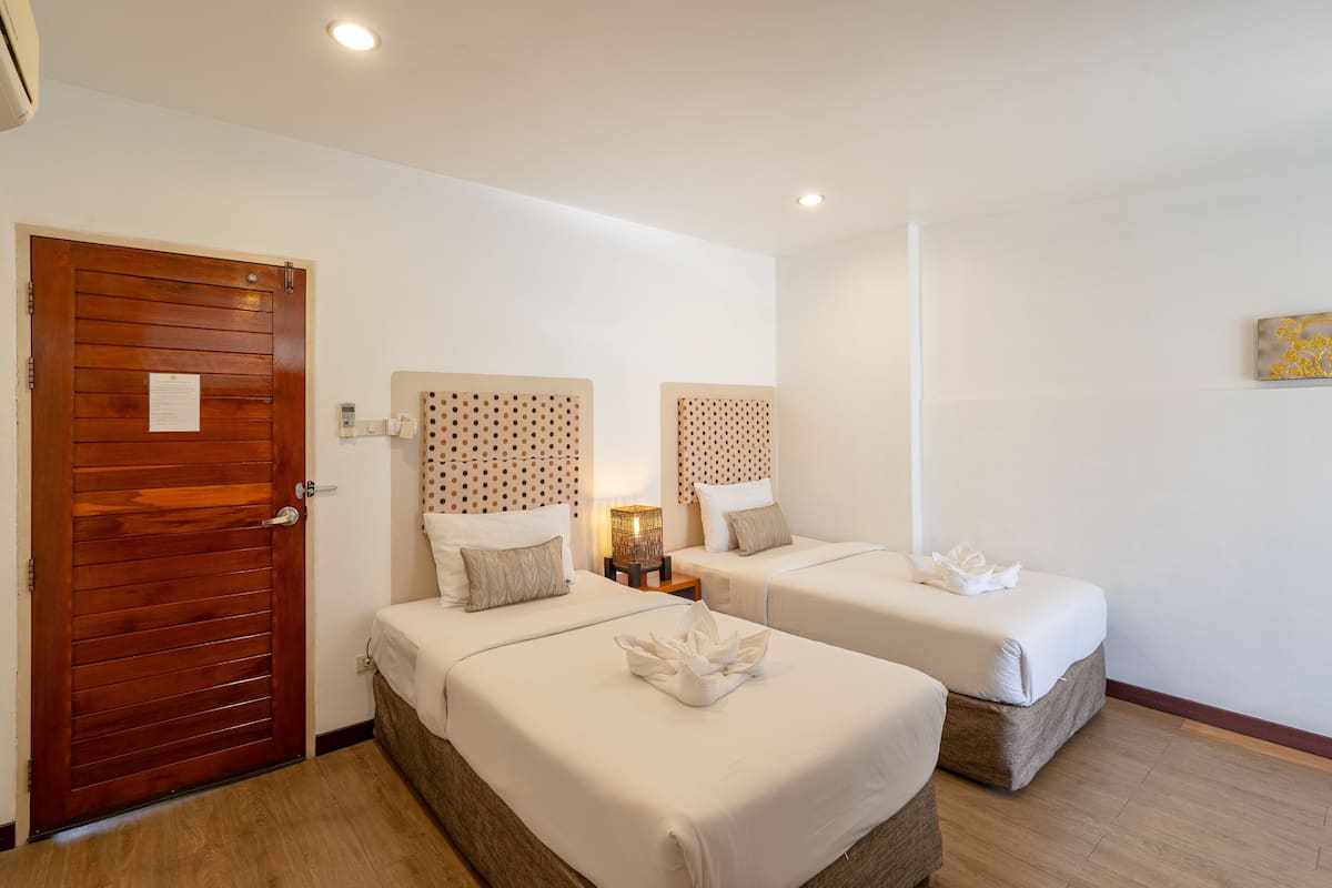 Una habitación de hotel con dos camas, una puerta de madera y una pequeña mesa con una lámpara.