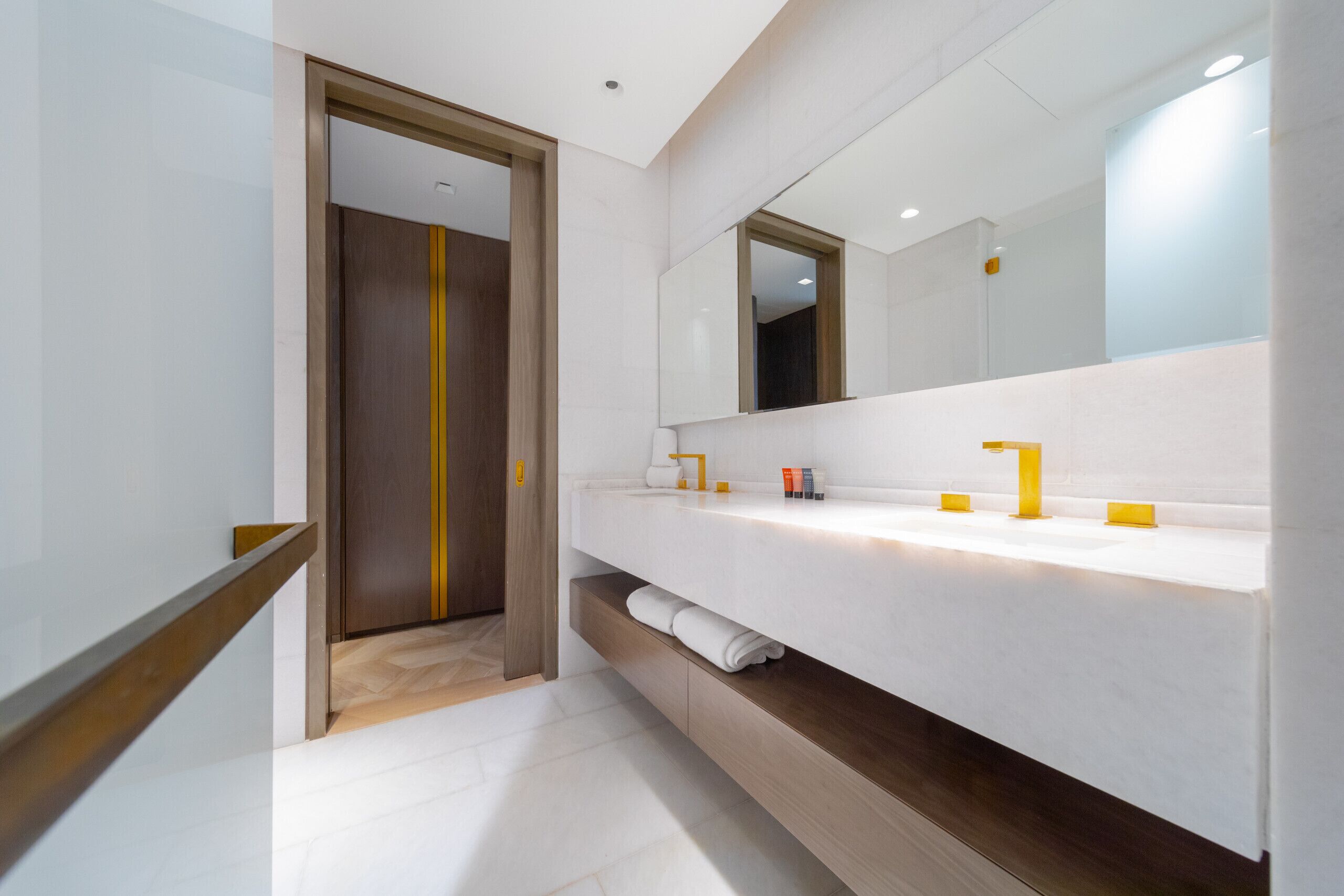 Un baño moderno con un espejo grande, encimera blanca y detalles de madera.