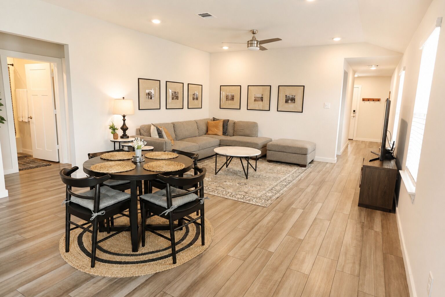 Un salon comprenant un canapé, une table basse, une table à manger avec des chaises et des tableaux encadrés accrochés au mur.