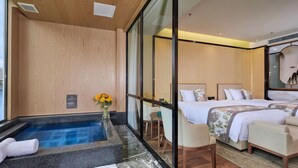 Ein Hotelzimmer mit großem Fenster und Blick auf ein Gewässer, ein Wellnessbereich mit Whirlpool und ein Bett mit Wasserblick.