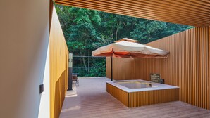 Ein moderner Außenbereich mit Holzterrasse, einem eingebauten Whirlpool und einem großen Sonnenschirm, der Schatten spendet.