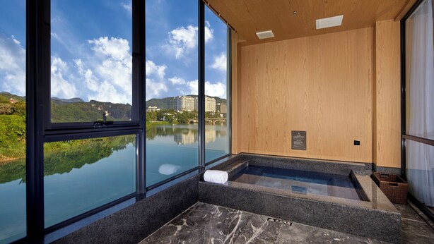 Ein moderner Wellnessraum mit großen Fenstern, einer Holzbalkendecke und Blick auf einen See und Gebäude.